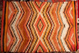 A Navajo flatweave rug, the serrated lozenge and chevron field in orange and vibrant colours,