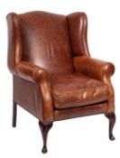 A 20th-century faux leather wingback armchair; with scrolled arms and removeable pad seat,