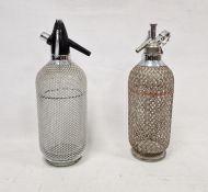Two vintage soda syphons within metal latticework casing