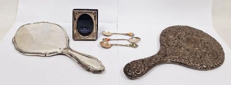 Two silver backed dressing mirrors, one repousse decorated, a miniature silver mounted picture frame