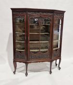 Edwardian mahogany display cabinet of canted form, the dentil cornice over a shell and acanthus
