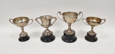 Four early 20th century unengraved silver trophies, each being twin-handled and raised on