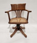 Early 20th century oak swivel desk chair, with hoop-shaped back and caned seat, on adjustable swivel