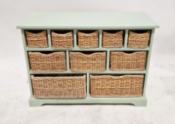 A contemporary painted storage unit comprising various compartments with wicker trays, measuring