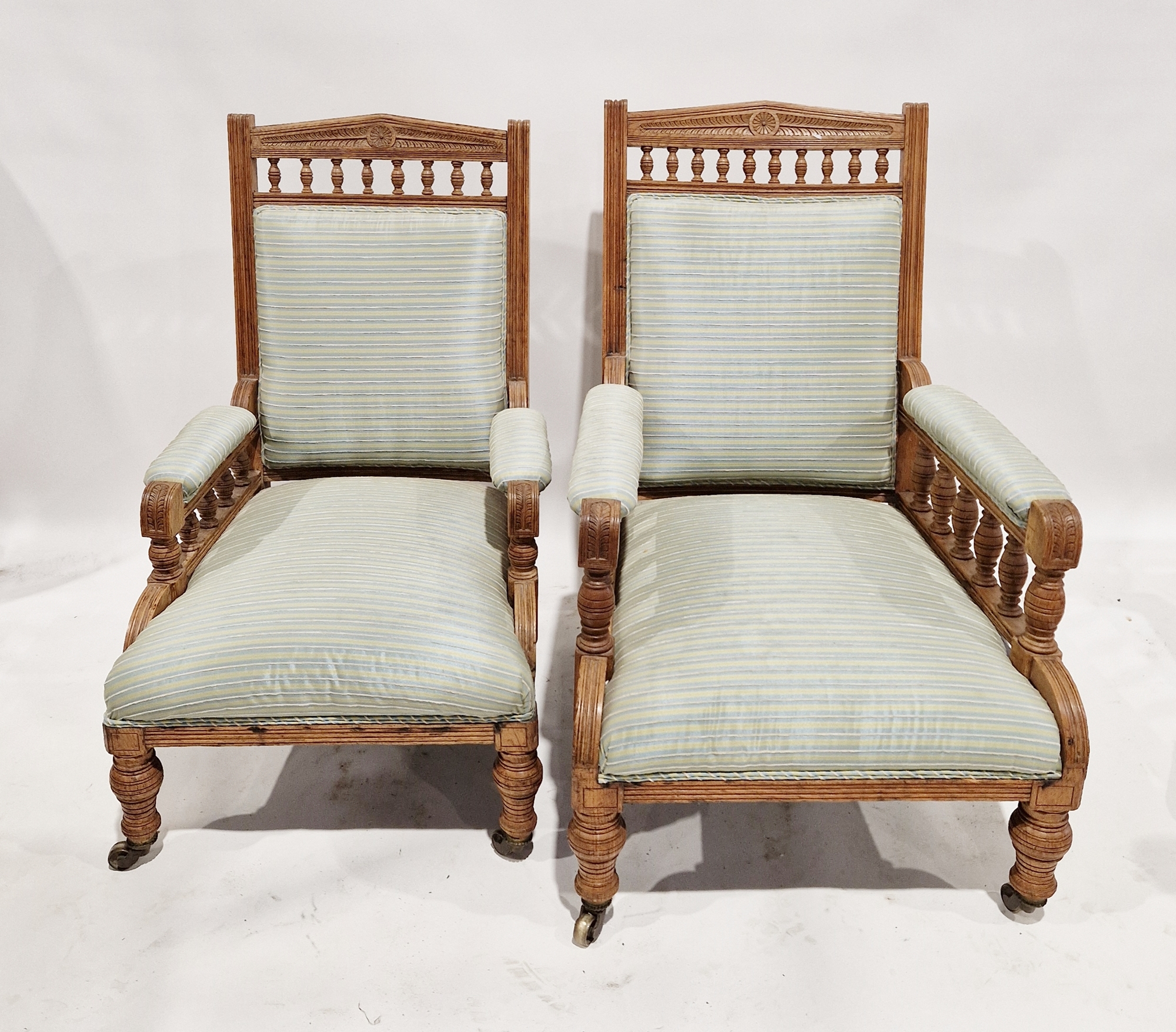 A matched pair of Edwardian oak armchairs each having upholstered seats, arms and back, largest