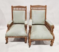 A matched pair of Edwardian oak armchairs each having upholstered seats, arms and back, largest