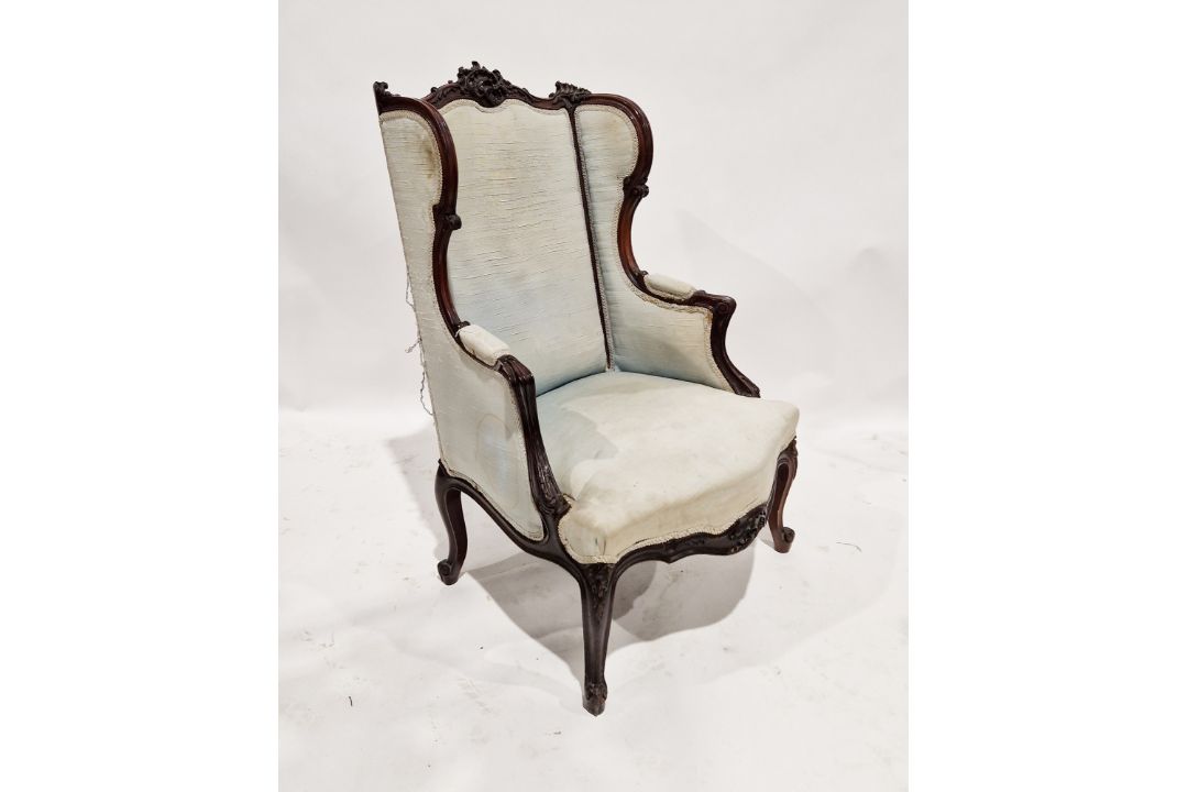 An antique mahogany wing backed armchair, having ornate carved scrolling decoration to the finial
