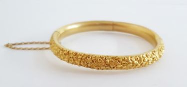 18ct gold bangle, all flowerhead embossed and with safety chain, 25g (repair to the centre of one