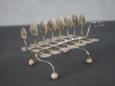 A Victorian naturalistic silver toast rack with lily pad design on four ball feet with engraved