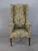 A 19th century wingback armchair, upholstered in tapestry style foliate fabric, raised on figured