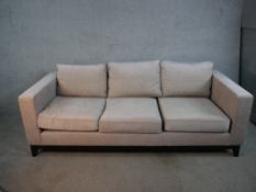 A contemporary three seater sofa, upholstered in light grey fabric, with angular arms, loose seat