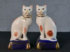 A pair of Staffordshire style pottery cats, each seated on a cobalt blue cushion with gilt