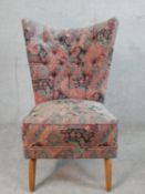 A mid 20th century light beech button back nursing chair, raised on out splayed supports.