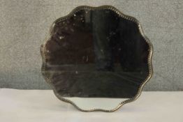 A 1930s scallop shaped and bevel edged mirrored stand, raised on squat ball feet. Dia.36cm.