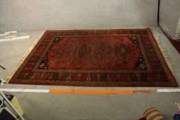 A late 19th century Persian woollen rug with stylised geometric motifs on a burgundy field within