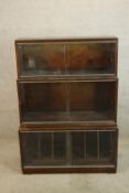 A mid 20th century three tier mahogany bookcase with glass sliding doors raised on shaped bracket
