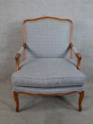 A 20th century beech framed French style open arm chair raised on carved cabriole supports