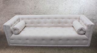 A contemporary white deep buttoned cotton upholstered sofa with cylindrical bolster cushions.