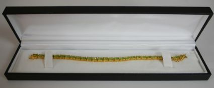 A boxed gold-plated silver peridot set tennis bracelet, set with twenty seven oval mixed cut