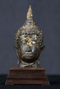 A 19th century bronze cast head of a buddha on a stepped hardwood plinth. With the remains of old