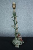 A metal lamp in the shape of a flower stem with a cherub seated at the base. Patinated and painted