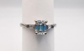 An Art Deco style 18ct white gold modern emerald cut diamond flanked solitaire ring. Set to centre