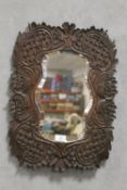 A CARVED WOODEN FRAMED BEVEL EDGED SHAPED WALL MIRROR