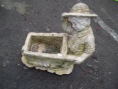 A CONCRETE GARDEN STATUE DEPICTING A BOY PUSHING A WHEEL BARROW
