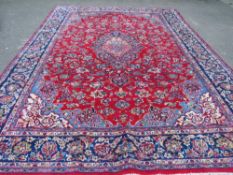 A LARGE CARPET WITH RED CENTRAL GROUND AND BLUE BORDER, APPROX 360 X 270 CM - WEAR THROUGHOUT