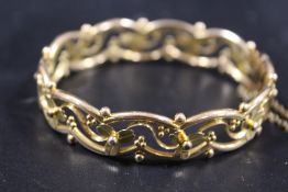 AN ORNATE CONTINENTAL YELLOW METAL BANGLE STAMPED 15 WITH DECORATIVE FLORAL WIREWORK DESIGN AND