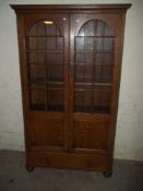 AN ANTIQUE SOLID OAK GLAZE LOCKING BOOKCASE WITH BUN FEET AND A LOWER DRAWER