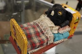 A VINTAGE TINPLATE BATTERY POWERED TOY BEAR RESTING IN A BED