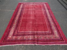 A LARGE RED GROUND WOOLLEN CARPET WITH PATTERNED BORDER APPROX 320 X 210 CM