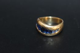 A HALLMARKED 18 CARAT GOLD SWIRL CHANNEL SET SAPPHIRE RING, set with 9 oval and circular