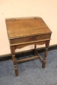 AN ANTIQUE OAK CLERKS DESK, the hinged lid opening to two shelves, raised on turned supports