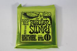 Twelve packs of Ernie Ball 2221 Regular Slinky Custom Gauge Electric Guitar Strings.
