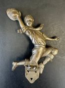 A car radiator badge in the form of a boy in pedal pushers and neckerchief, waving a hat with his