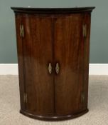 GEORGIAN MAHOGANY BOW FRONT WALL HANGING CORNER CUPBOARD, having twin opening doors with fancy brass