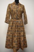 A late 1950s cotton day dress, having geometric pattern in brown and blue hues, belt to waist and