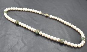 A pearl and green stone necklace, having numerous pearl beads interspersed by five green stone