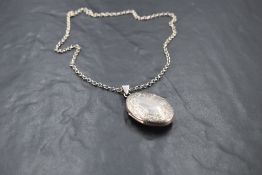 A silver locket of oval form having engraved scroll decoration on a 17' silver belcher chain