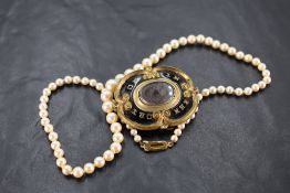 A Victorian mourning brooch bearing a central hair locket in a black enamel and pinchbeck mount, and