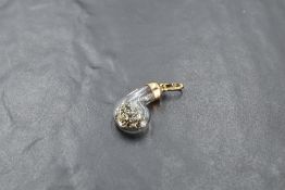 A yellow metal and glass pendant, of 'b' shape and containing jewellers lathe shavings, the