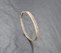 A yellow metal diamond set bangle, of hinged oval form having a linear arrangement of seventeen