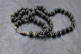 A string of Jade style dark green beads of even form, approx 23'