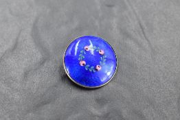 A silver brooch of circular form having blue enamel guilloche rose and briar decoration,