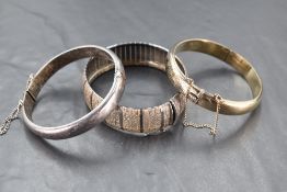 Two silver hinged bangles having similar engraved scroll decoration and a silver articulated cuff