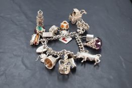 A silver and white metal charm bracelet, the curb type links suspending a variety of charms,