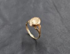 A 9ct gold locket ring, the oval hinged matrix with engraved scrolling decoration, all between V-