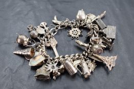 A silver charm bracelet having 34 white metal and silver charms including Eiffel tower, cowbell etc,